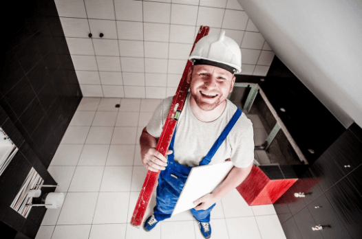 Smiling tiler in a hard hat standing in a newly tiled bathroom