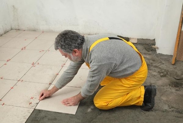 Tiler marking out and laying square floor tiles with a spacer grid