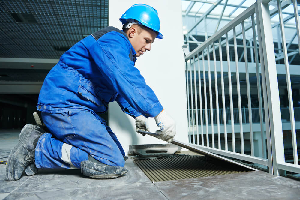Tiler in blue overalls installing outdoor floor tiles on a commercial balcony