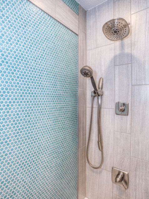 Shower wall with teal penny-round mosaic tiles beside a rain showerhead
