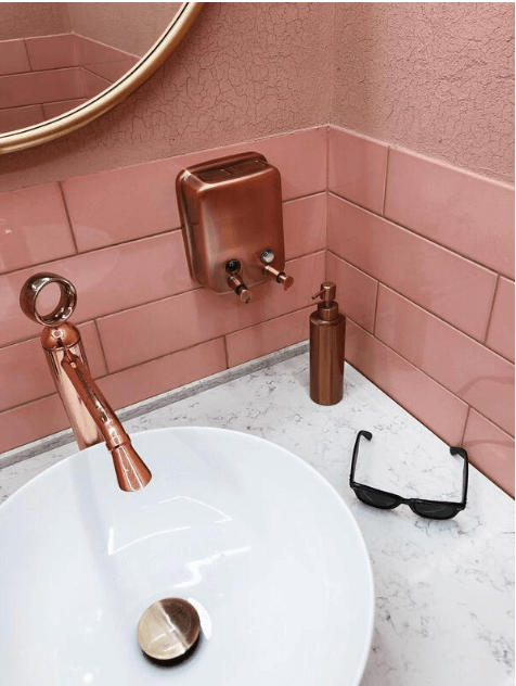 Pink gloss subway wall tiles behind a copper basin tap in a powder room