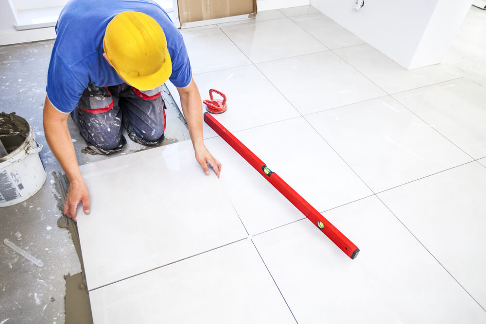 Tiler in a hard hat laying large white floor tiles using a spirit level