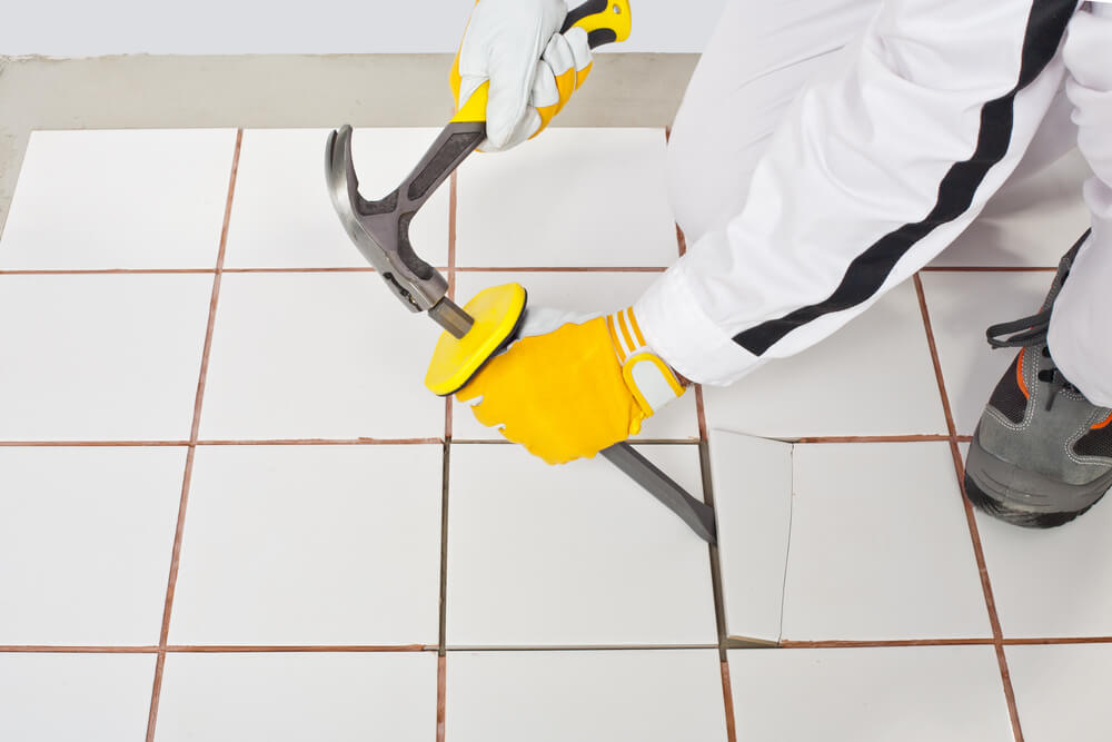Tiler using a hammer and chisel to remove old white floor tiles