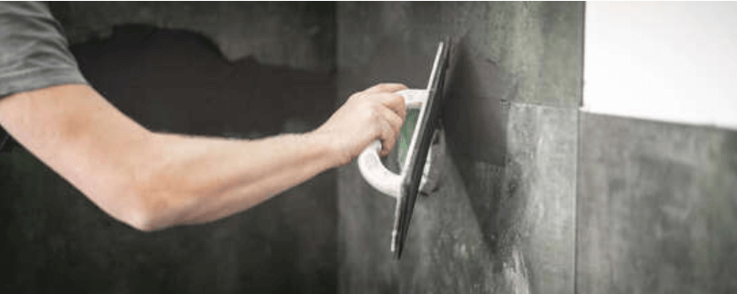 Tiler smoothing adhesive across a wall before laying tiles