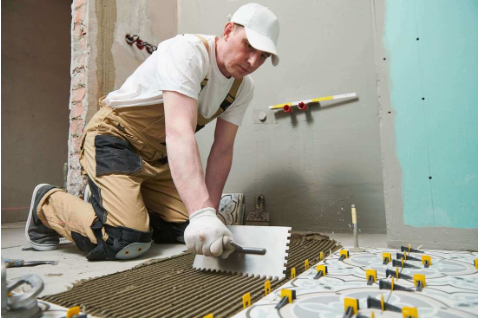 Tiler spreading adhesive with a notched trowel before laying floor tiles