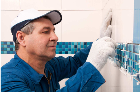 Tiler fitting white wall tiles above a teal mosaic border strip