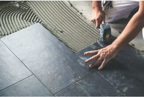 Close-up of a tiler fitting a dark slate floor tile into a bed of adhesive