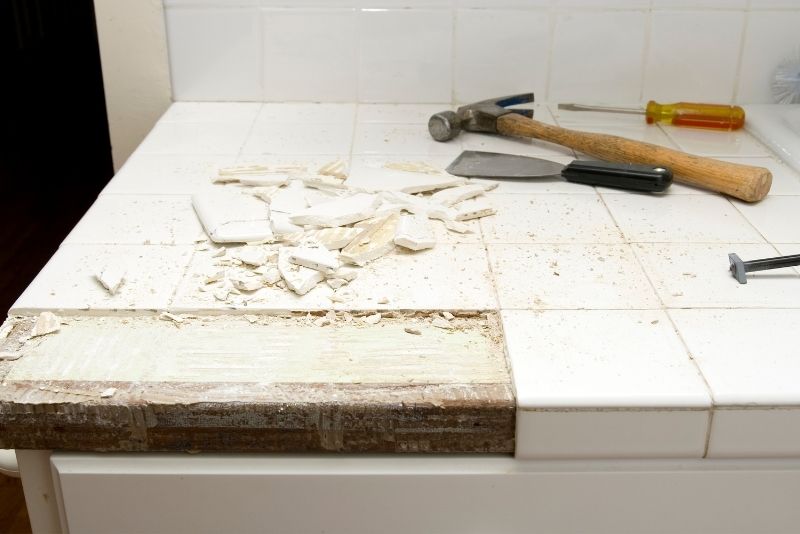 Old tiles being chiselled off a kitchen benchtop during removal